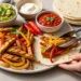 Quick chicken fajitas with colorful peppers, onions, tortillas and fresh toppings on rustic wooden table