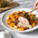 One-pan roasted pork tenderloin with fall root vegetables, carrots, and sweet potatoes on a dark baking sheet.