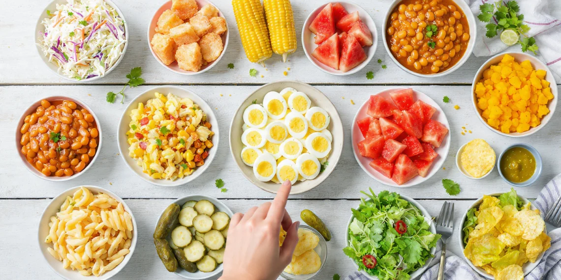A spread of 15 colorful cookout side dishes including pasta salad, coleslaw, and grilled vegetables on a picnic table